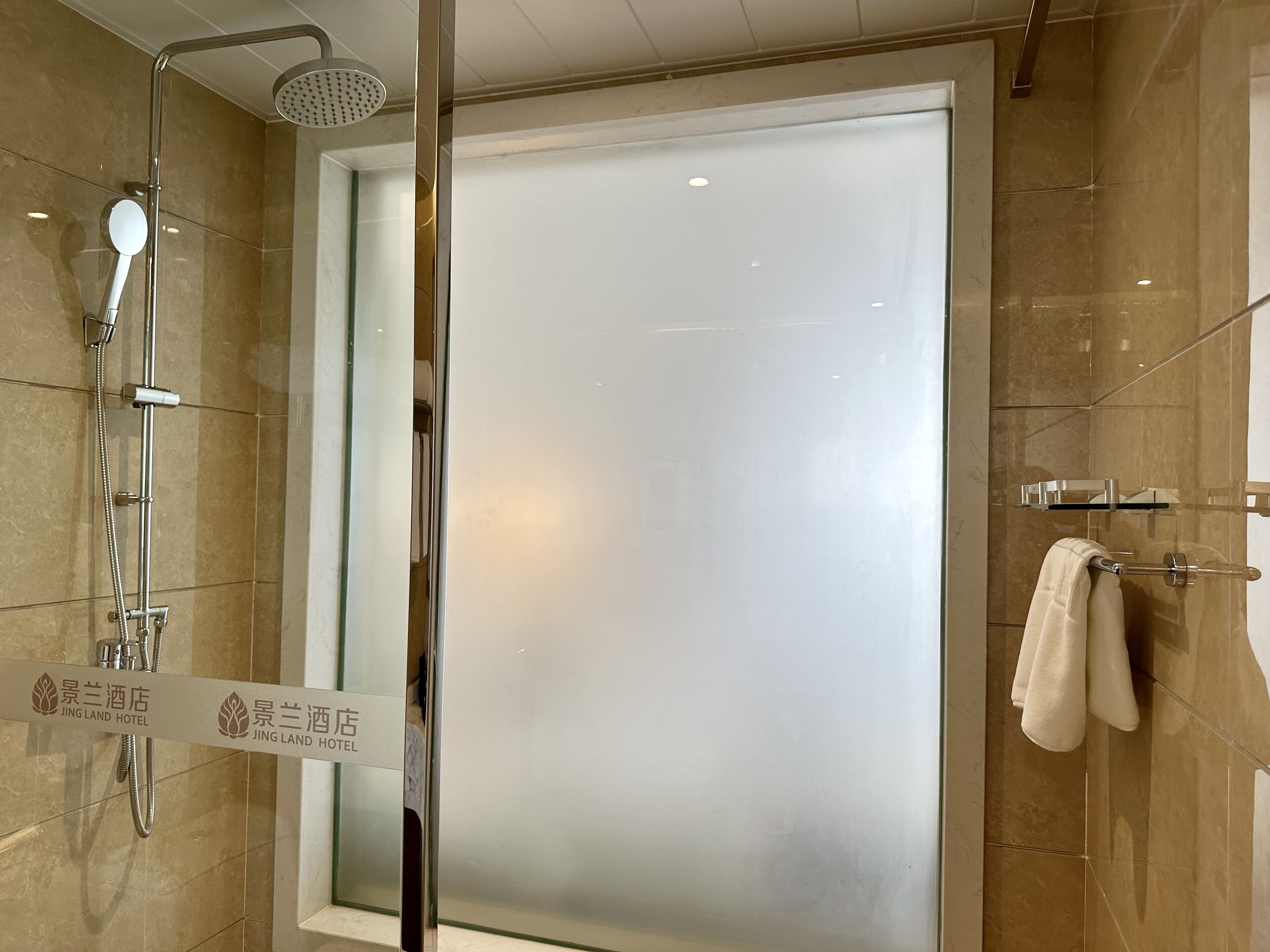 Une salle de bain moderne dotée d’une douche à parois de verre, d’un porte-serviettes apparent et d’une enseigne indiquant qu’il s’agit de l’hôtel Jing Land.