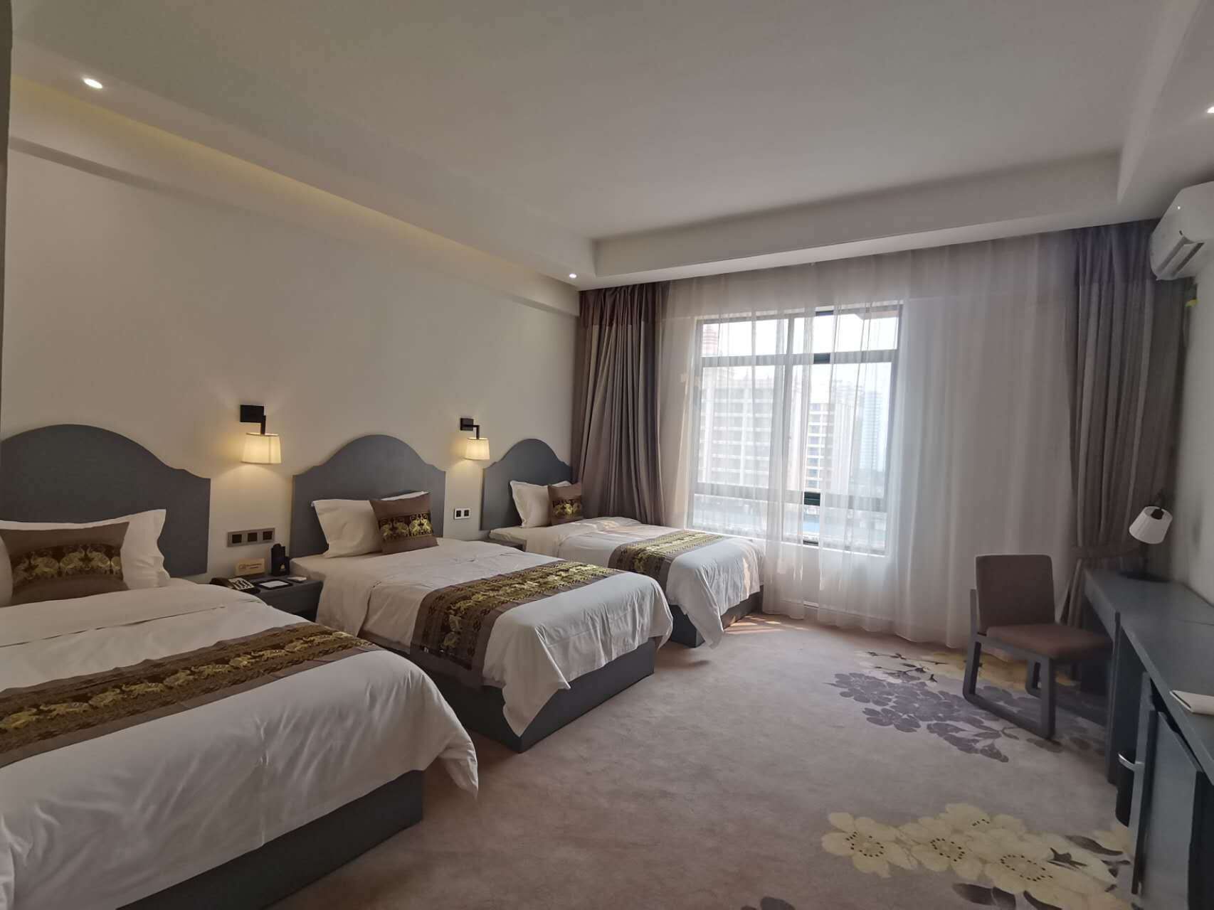 Ein Hotelzimmer mit drei Betten, einem Schreibtisch und einem Sessel.