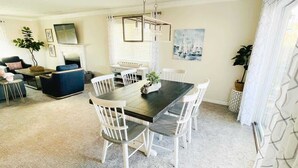 Un coin repas avec une table en bois foncé et des chaises blanches, un lustre et un tableau représentant des voiliers accroché au mur.