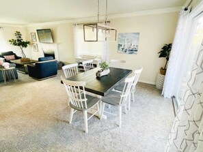 A dining area with a dark wooden table and white chairs, a chandelier, and a painting of sailboats on the wall.