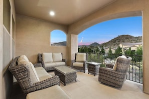 A balcony with wicker furniture, a view of hills, and a clear sky.
