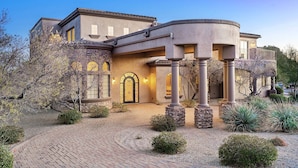 A large, modern house with a curved entrance, stone pillars, and a well-maintained garden with various plants. - Luxury Oasis Heated Pool & Spa* - 7BR Luxury Estate w/ Panoramic Mountain Views! (Mesa)