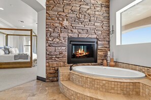 Un baño moderno con pared de piedra, chimenea y bañera independiente.