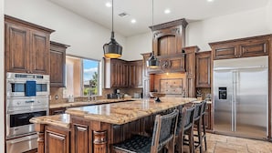 A kitchen with wooden cabinets, a large island, bar stools, a stainless steel refrigerator, and pendant lighting. - Luxury Oasis Heated Pool & Spa* - 7BR Luxury Estate w/ Panoramic Mountain Views! (Mesa)