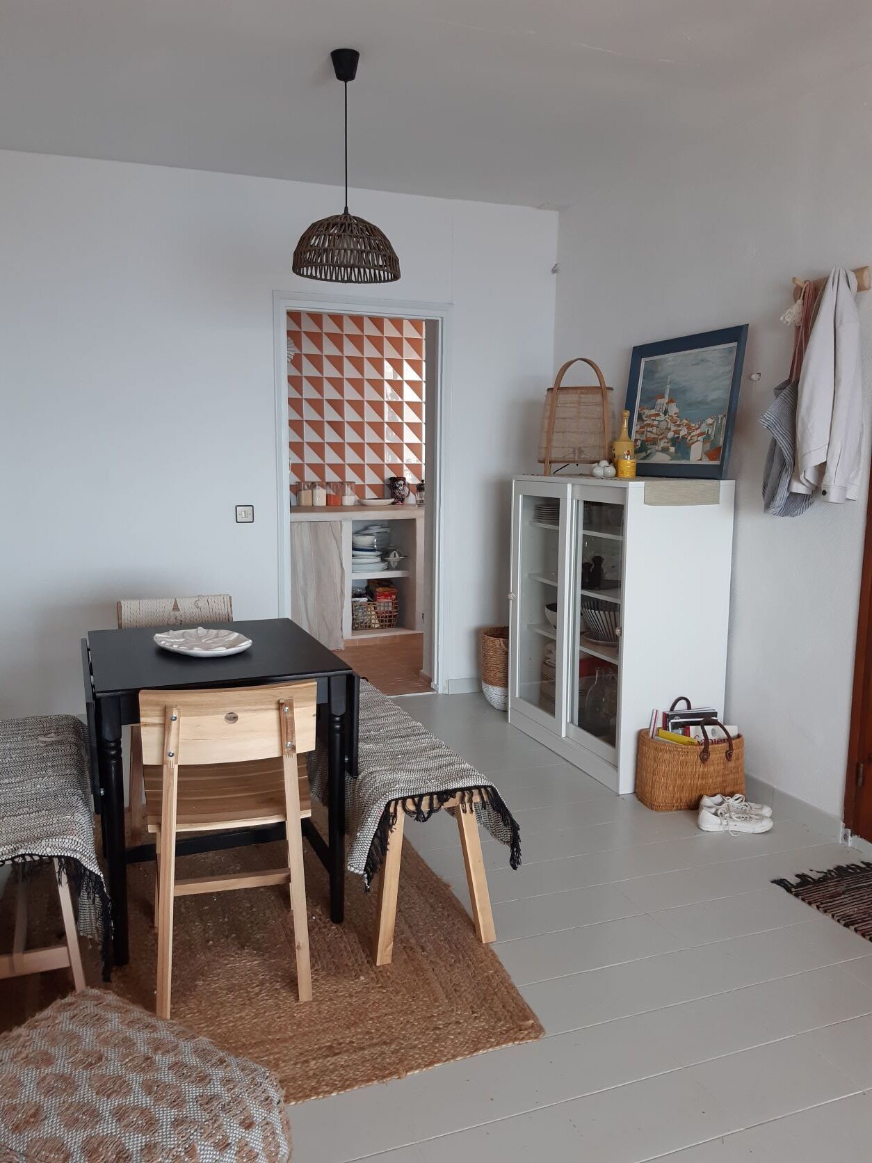 Een eetruimte met een tafel, stoelen, een hanglamp, een kast met glazen deuren en een aan de muur hangend schilderij.