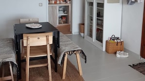 Un espace repas comprenant une table, des chaises, un luminaire suspendu, un meuble avec des portes en verre et un tableau accroché au mur.