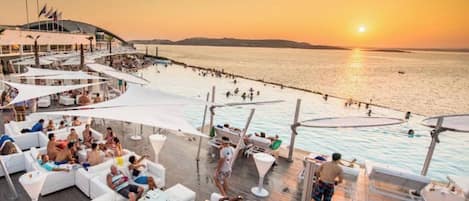 A rooftop bar with outdoor seating and a view of the sea at sunset.