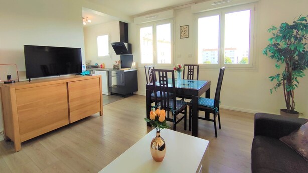 A modern living room with a flat-screen TV, wooden cabinet, dining table with chairs, and a potted plant.