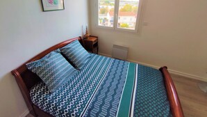 A bedroom with a bed, a nightstand, a window with a view of buildings, and a radiator.