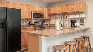 Una cocina moderna con armarios de madera, un refrigerador negro, electrodomésticos de acero inoxidable, una encimera de mármol y taburetes de madera.
