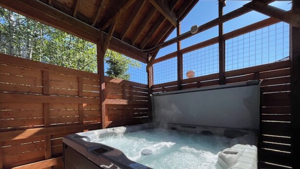 Un jacuzzi con cubierta de madera y estructura metálica, rodeado por una valla de madera.