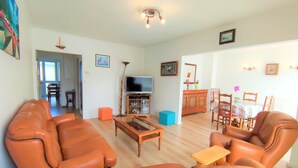 A living room with leather sofas, a wooden coffee table, a TV, and a dining area with a table and chairs.