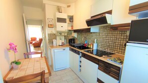 A compact kitchen with a small refrigerator, a sink, and a microwave. There is a dining table with chairs and a potted plant.