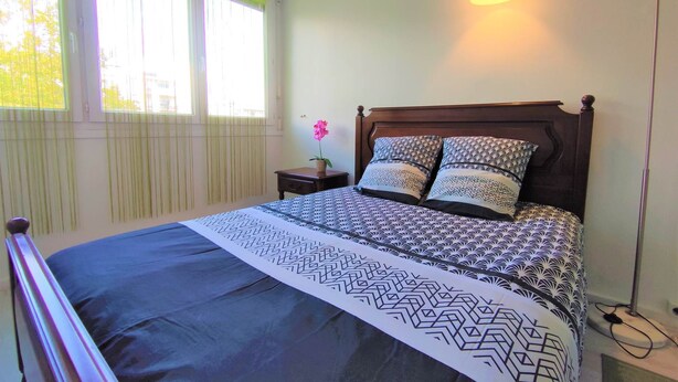 A neatly made bed with patterned bedding, a bedside table with a flower, and a floor lamp.