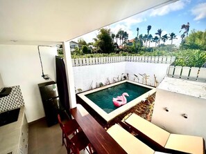 A small pool with a flamingo float, a refrigerator, a dining table with chairs, and a view of palm trees and houses. - Canggu Jungle View Villa (Canggu)