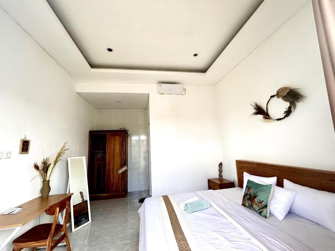 A hotel room with a bed, a desk, and a chair. There is a mirror on the wall and a door leading to another room.