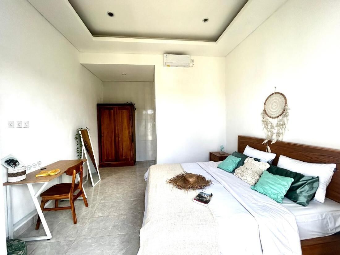 A bedroom with a bed, a desk, and a chair. There is a dreamcatcher on the bed and a mirror on the wall.