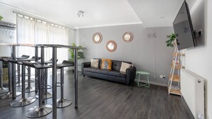 A modern living room with a grey sofa, a dining area with bar stools, and a mounted TV. - Get Away Home With Hot Tub Sleeps 4 (Peacehaven)