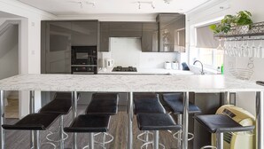 A modern kitchen with a marble countertop, black bar stools, and a built-in oven. - Get Away Home With Hot Tub Sleeps 4 (Peacehaven)