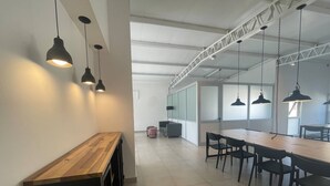 Un espacio de oficina moderno con una larga mesa de madera y sillas negras, iluminación suspendida y un techo alto con vigas a la vista.