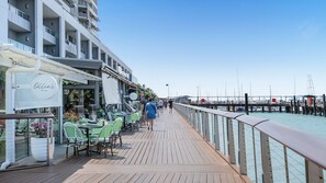 A wooden deck with outdoor seating, a restaurant named "Ollie's Italian," and a marina with boats in the background.