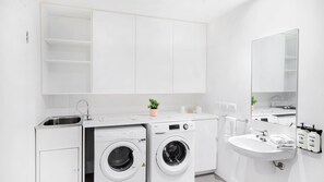 A modern, white bathroom with a built-in washing machine, a sink, and a mirror.