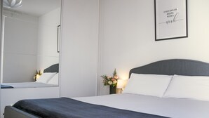 Ein modernes Hotelzimmer mit einem großen Bett, einem Nachttisch mit Lampe, einem gerahmten inspirierenden Zitat an der Wand und einem Spiegel, der den Raum reflektiert.