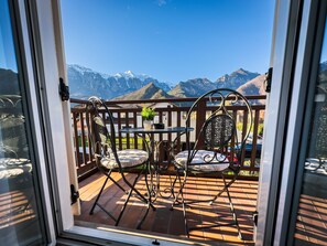 A balcony with two chairs and a table, offering a view of snow-capped mountains.