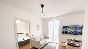 Ein modernes Wohnzimmer mit einer Couch, einem Esstisch für zwei Personen und einem großen Wandfernseher.