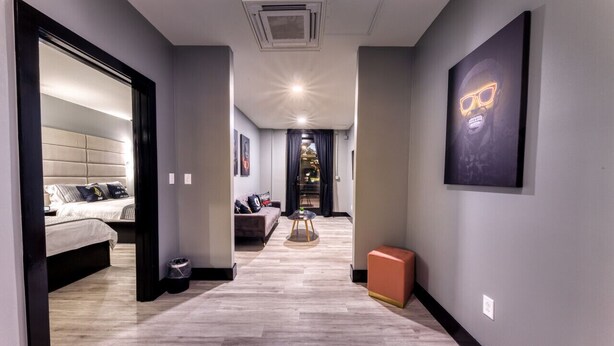 A modern hallway with a bed, a sofa, a small table, and a framed picture on the wall. - The Bella Downtown`s Young Money Manor Suite, 2 Queen Beds, Sleeps 4 (Biloxi)