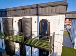 Un bâtiment moderne avec une façade en briques blanches, de grandes fenêtres en arc de cercle et un balcon recouvert d’un gazon artificiel vert.