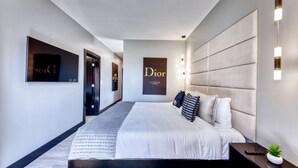 Ein modernes Hotelzimmer mit einem großen Bett, einem Kopfteil, einem Nachttisch und einer kleinen Pflanze.
