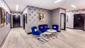 Eine Hotelhalle mit modernem Design, mit Marmorboden, blauen Sesseln, einem runden Tisch und einem großen gerahmten Kunstwerk an der Wand.