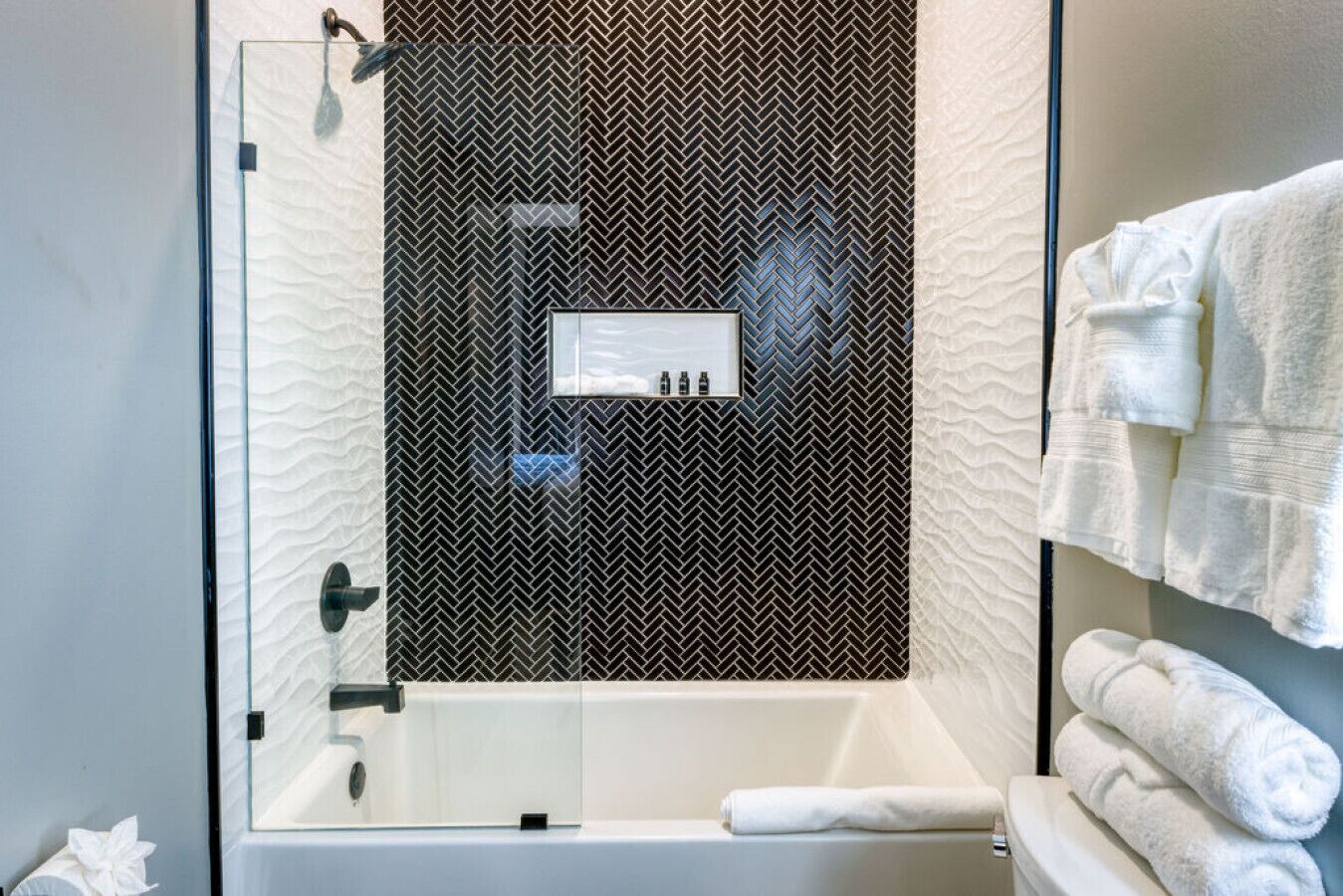 Ein modernes Badezimmer mit einer gläsernen Dusche, einer Wand mit Zickzackmuster und ordentlich gefalteten Handtüchern.