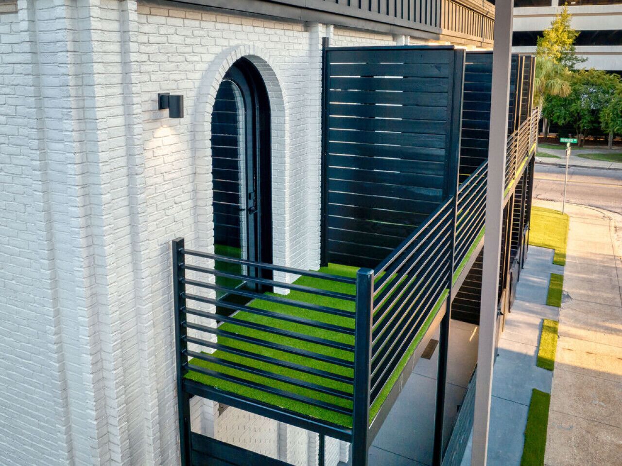 A modern building with a white brick facade, a black metal staircase, and a green artificial grass balcony.