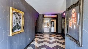 Un couloir avec un papier peint à motifs, un sol à chevrons et des tableaux encadrés accrochés aux murs.