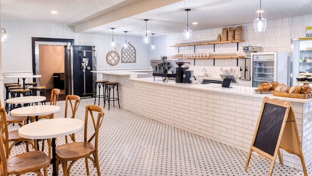 Un café avec un comptoir, des tables, des chaises et un panneau d’affichage noir.
