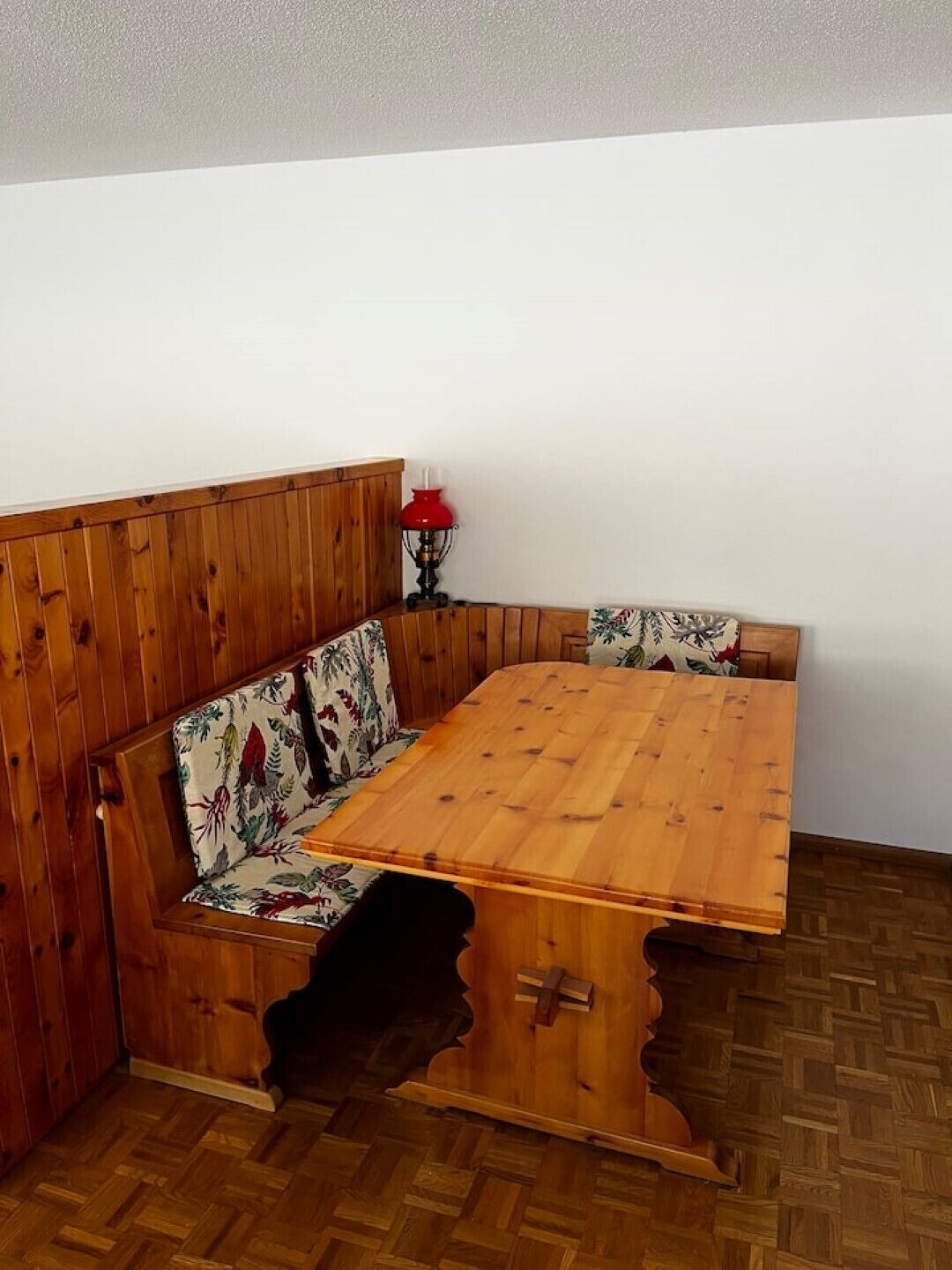 A wooden dining table with a bench, a red lamp, and a patterned cushion.