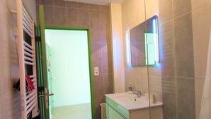 Uma casa de banho moderna com cabine de duche em vidro, lavatório branco com espelho e toalheiro com toalhas dobradas.