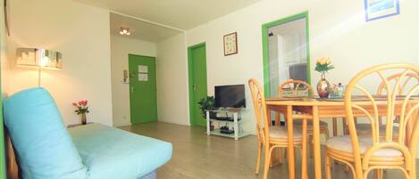 A living room with a blue sofa, wooden dining table with chairs, a TV, and a green door.
