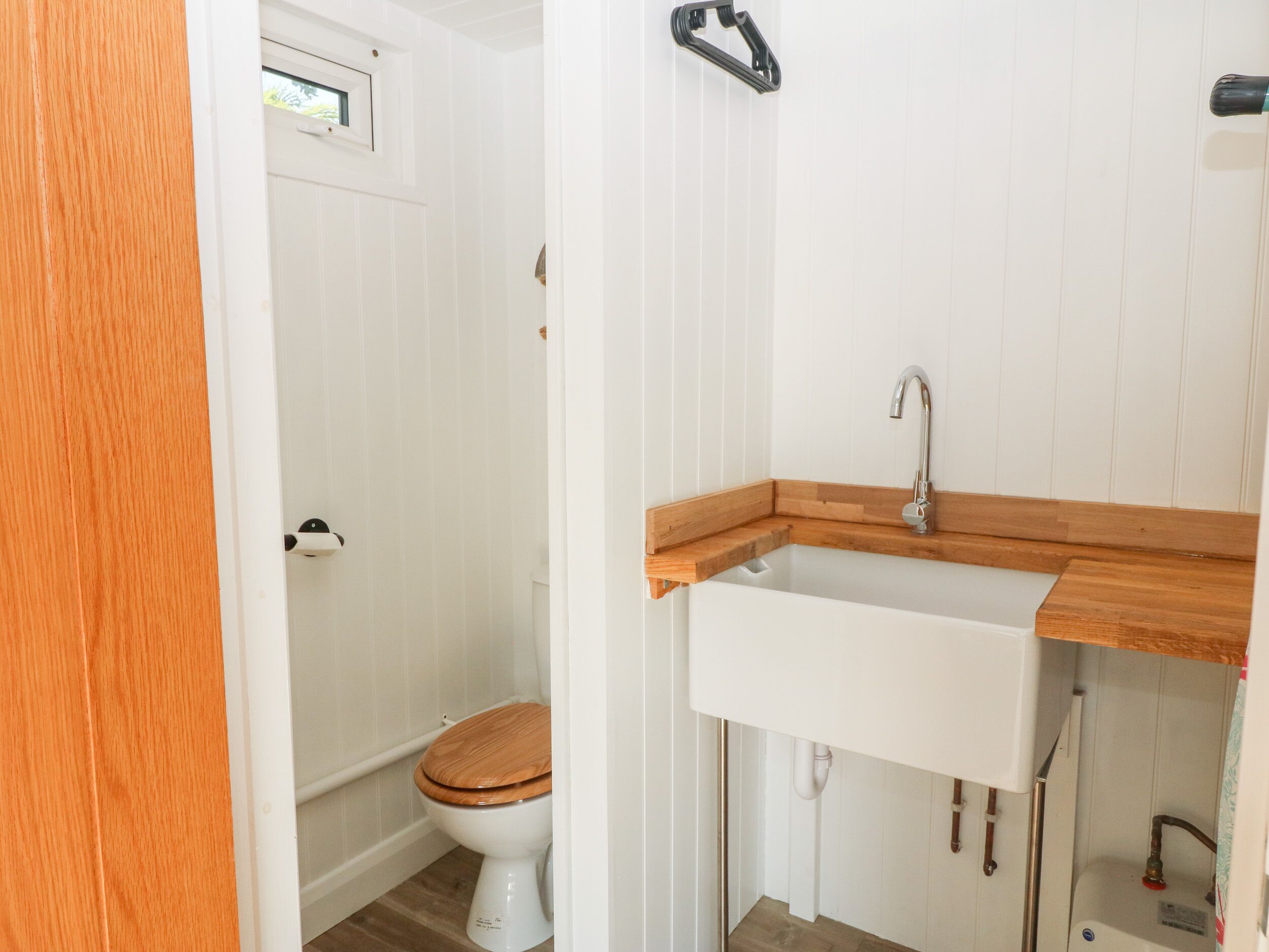 Une salle de bain avec un meuble-lavabo en bois, des accessoires blancs et une fenêtre située au-dessus des toilettes.