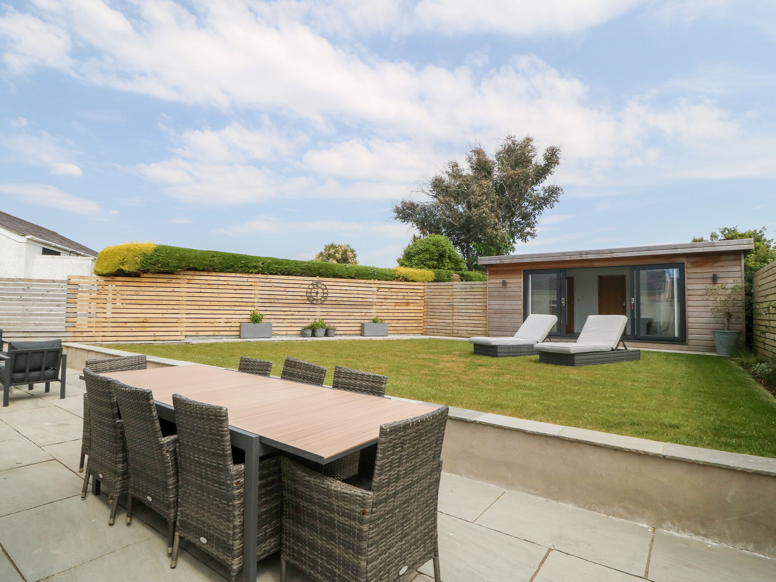 A backyard with a dining table and chairs, a small seating area with lounge chairs, a wooden fence, and a modern building with large windows.