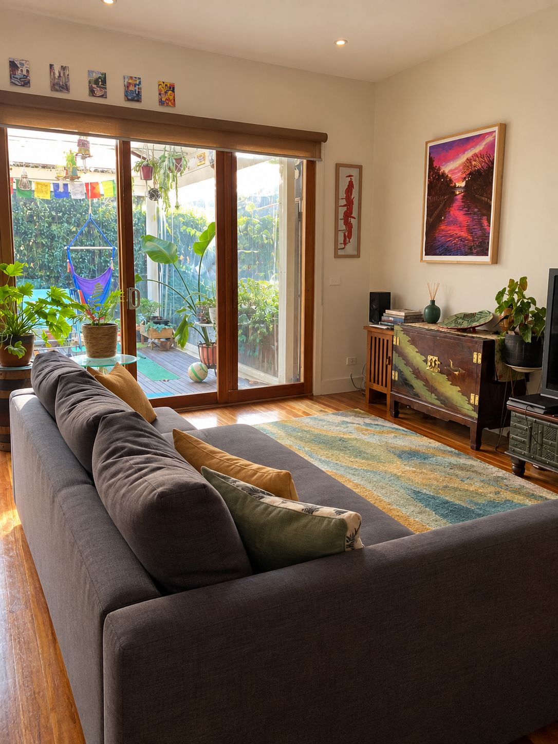 Un salon comprenant un canapé, un téléviseur et une porte-fenêtre coulissante donnant sur un balcon agrémenté de plantes.