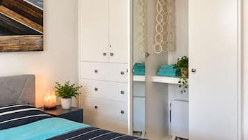 Une chambre à coucher avec un lit, une table de chevet avec une lampe, une armoire avec un miroir et une plante.