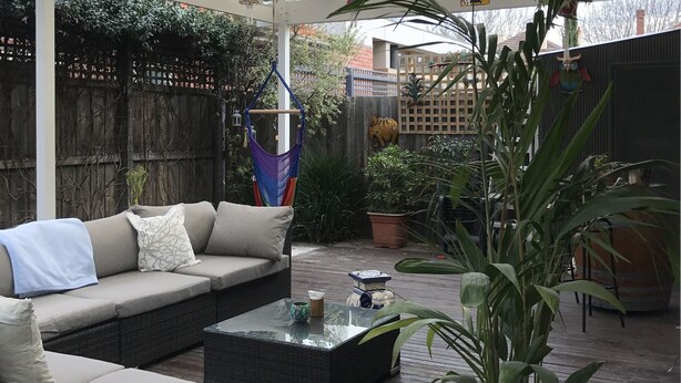 An outdoor patio with a covered seating area, a potted plant, and hanging decorations.
