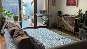 A spacious living room with a large bed, a desk with a keyboard, and a painting on the wall.