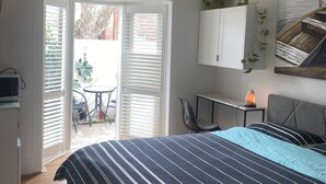 A bedroom with a bed, a ceiling fan, a desk, a chair, a heater, and a sliding glass door leading to an outdoor area.
