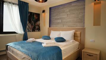 Habitación de hotel con una cama grande, una mesita de noche, una lámpara de pared y un ventanal con cortinas.