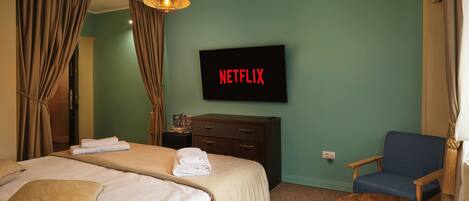 Una habitación de hotel con una cama, una silla, un televisor mostrando "NETFLIX" y una mesita de madera.
