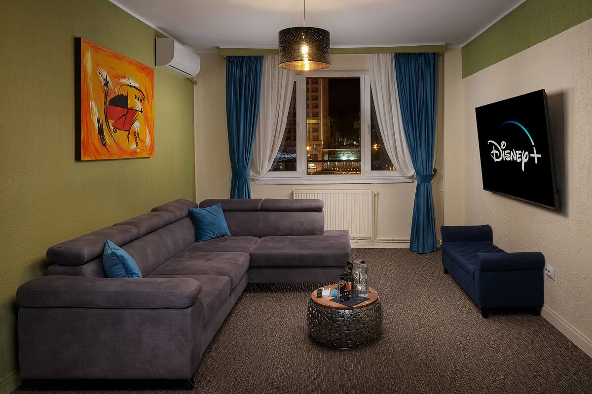 A living room with a sectional sofa, a small round coffee table, a flat-screen TV, and a painting on the wall.